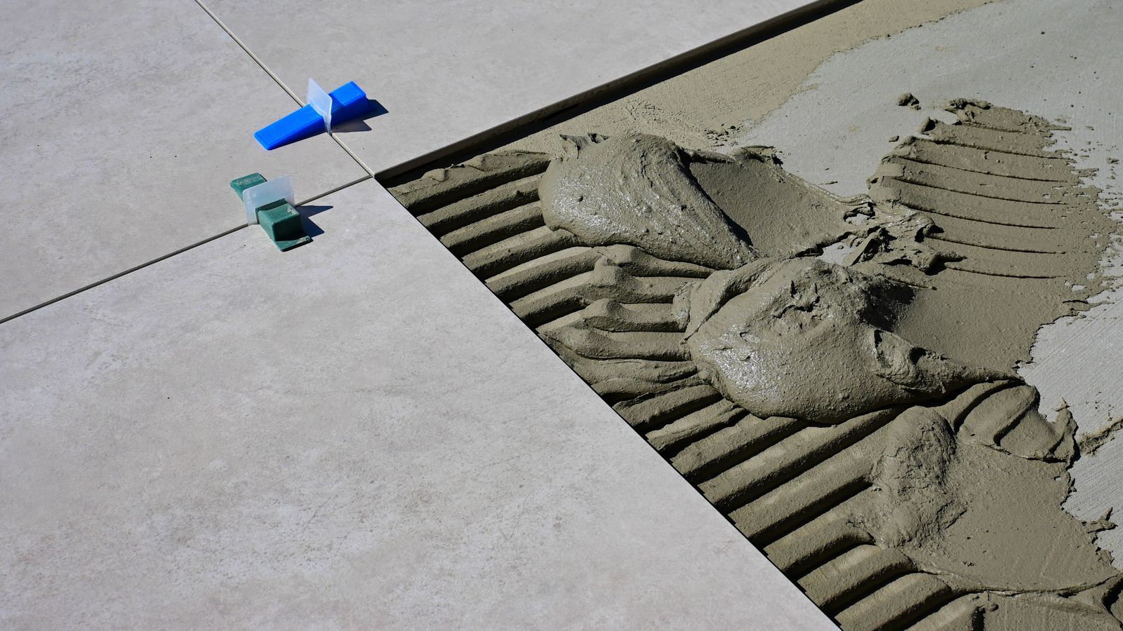 Close-up of wet cement and tile spacers during floor tile installation.