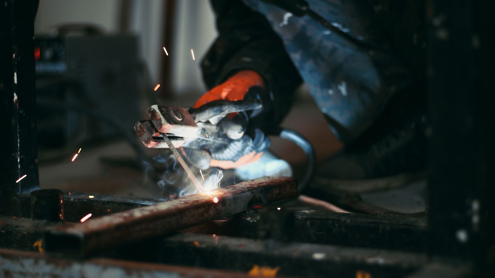 Focused shot of a welder's hands holding an electrode while sparks fly during metalwork.