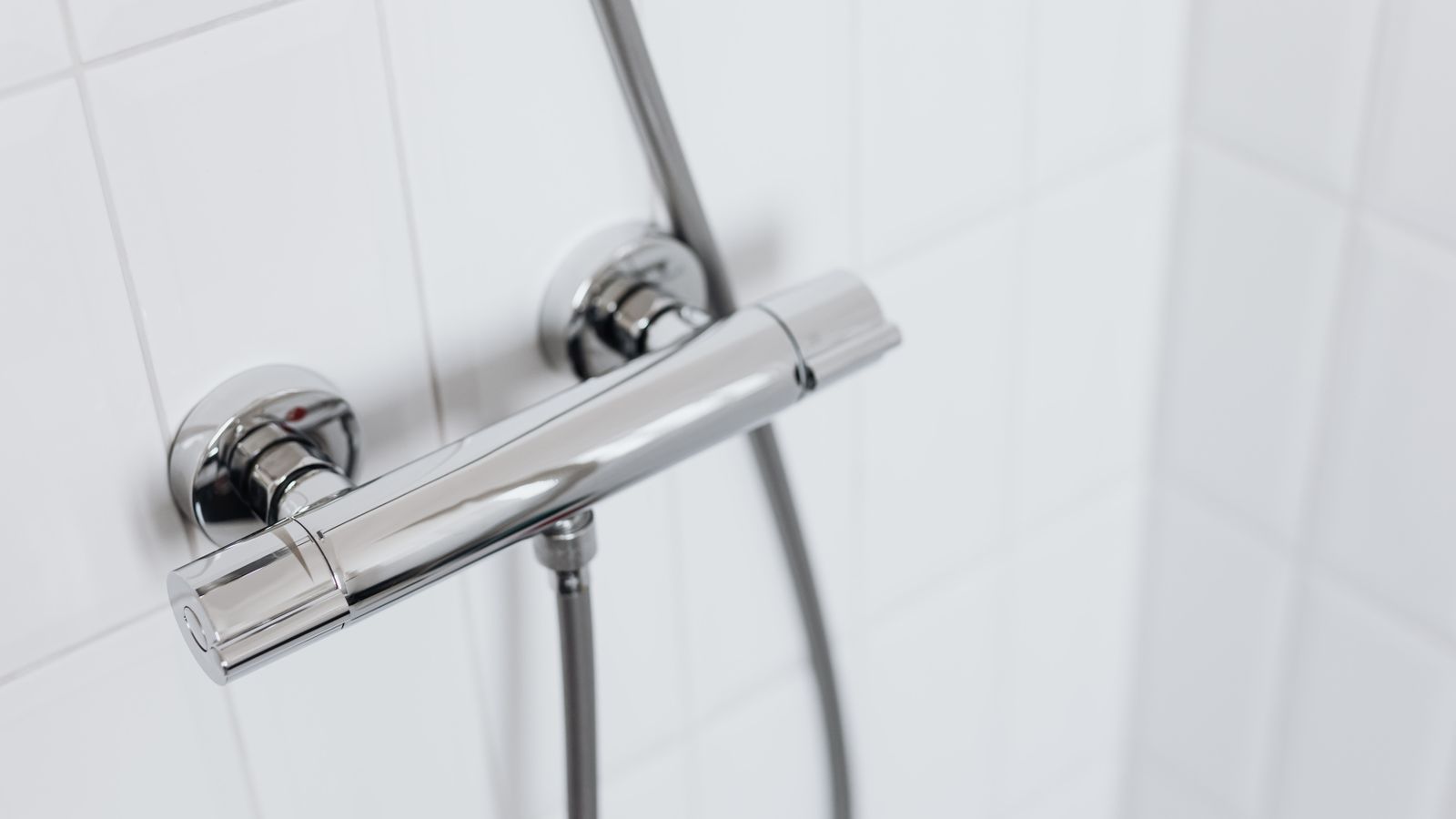 Modern chrome shower faucet on white tiled wall, elegant and clean design.